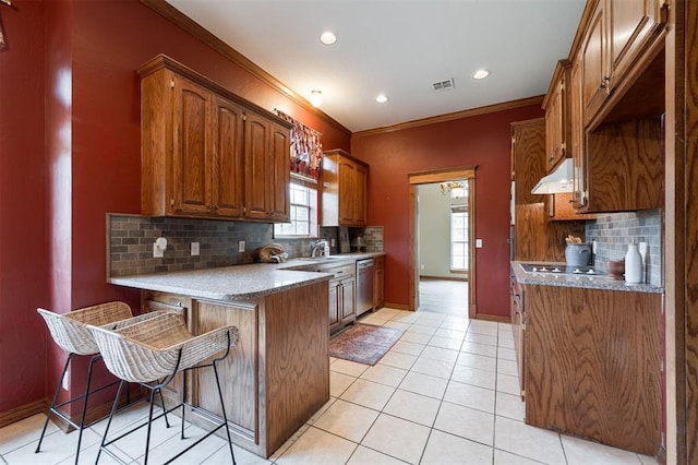 1723 Grey Hawk Rd, Edmond, OK 73003 - kitchen with under cabinet range hood, stainless steel dishwasher, a peninsula, backsplash, and brown cabinetry