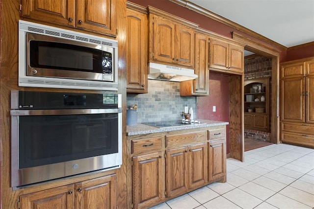 1723 Grey Hawk Rd, Edmond, OK 73003 - kitchen featuring appliances with stainless steel finishes, under cabinet range hood, light tile patterned flooring, brown cabinetry, and backsplash
