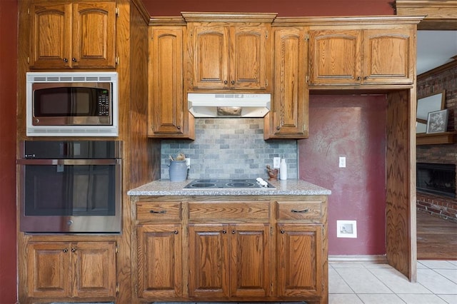 1723 Grey Hawk Rd, Edmond, OK 73003 - kitchen with stainless steel appliances, under cabinet range hood, brown cabinets, light tile patterned floors, and backsplash