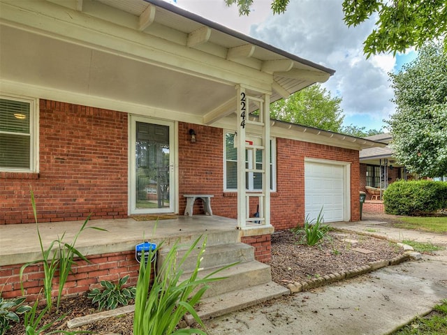 2244 Downing St, Oklahoma City, OK 73120 - view of exterior entry with a garage, a porch, driveway, and brick siding