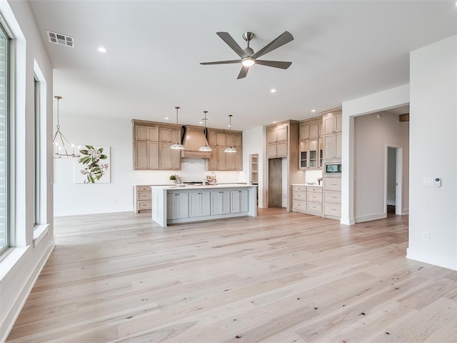 208 Pont Neuf Ct, Edmond, OK 73034 - kitchen with custom range hood, stainless steel microwave, ceiling fan, light wood-style flooring, and a kitchen island with sink