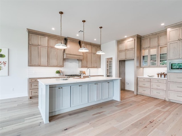 208 Pont Neuf Ct, Edmond, OK 73034 - kitchen with custom range hood, decorative backsplash, light wood-style flooring, light countertops, and stainless steel microwave