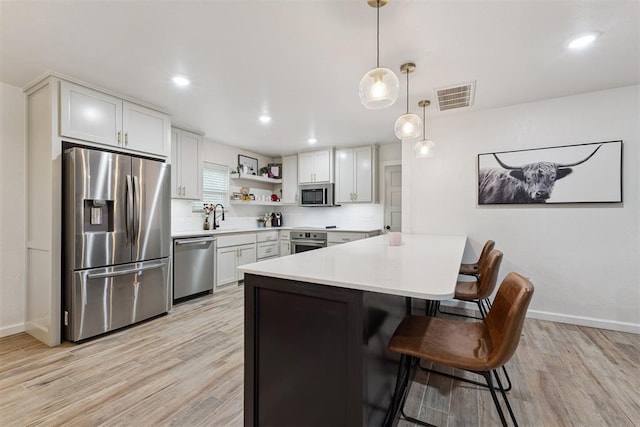 8 Corona Dr, Oklahoma City, OK 73149 - kitchen featuring stainless steel appliances, a peninsula, light wood finished floors, a breakfast bar area, and open shelves