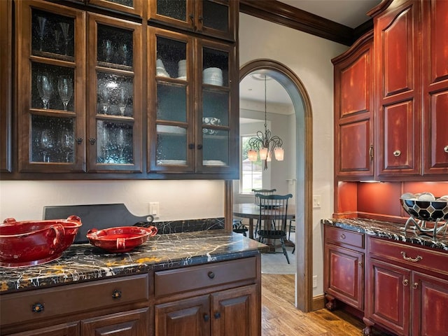 3325 Winding Creek Cir, Edmond, OK 73034 - kitchen featuring ornamental molding, light wood-style floors, glass insert cabinets, arched walkways, and dark stone countertops