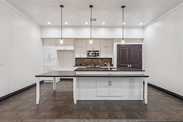 2429 NW 176th St, Edmond, OK 73012 - kitchen featuring stainless steel microwave, dark countertops, white cabinetry, tasteful backsplash, and a center island with sink
