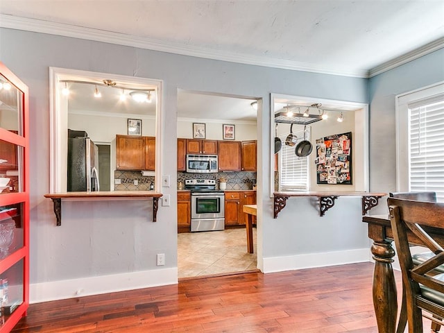 1122 NW 42nd St, Oklahoma City, OK 73118 - kitchen with stainless steel appliances, brown cabinetry, backsplash, light wood-style floors, and crown molding