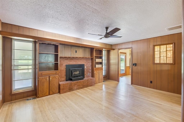 13722 NE 9th St, Choctaw, OK 73020 - unfurnished living room featuring wood finished floors, a ceiling fan, a textured ceiling, wood walls, and a wood stove