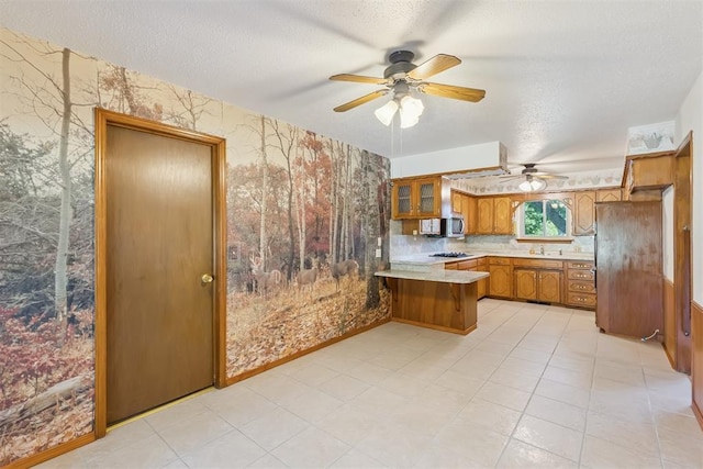 13722 NE 9th St, Choctaw, OK 73020 - kitchen featuring a peninsula, wallpapered walls, a textured ceiling, a ceiling fan, and brown cabinets