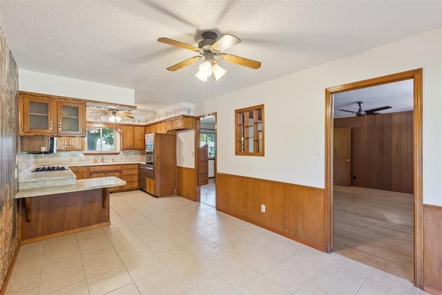 13722 NE 9th St, Choctaw, OK 73020 - kitchen featuring ceiling fan, brown cabinetry, wooden walls, black gas cooktop, and a peninsula
