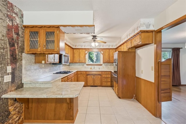 13722 NE 9th St, Choctaw, OK 73020 - kitchen featuring brown cabinetry, a peninsula, light countertops, ceiling fan, and glass insert cabinets