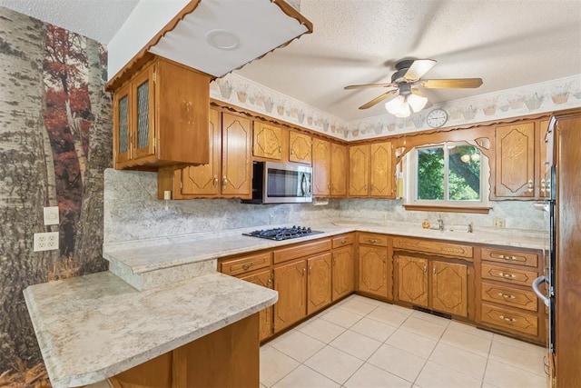 13722 NE 9th St, Choctaw, OK 73020 - kitchen with stainless steel microwave, a peninsula, black gas stovetop, brown cabinetry, and light countertops
