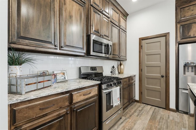 13 Ivory Dr, Yukon, OK 73099 - kitchen with appliances with stainless steel finishes, light wood-style floors, decorative backsplash, dark brown cabinetry, and light stone countertops