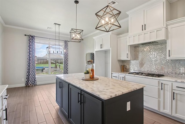 12825 SW 26th St, Yukon, OK 73099 - kitchen with white cabinets, tasteful backsplash, a center island, ornamental molding, and wood finished floors