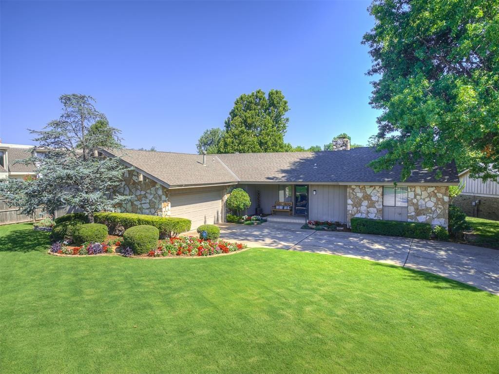 3305 Brookhollow Rd, Oklahoma City, OK 73120 - view of front of house featuring stone siding, a front lawn, an attached garage, a chimney, and driveway