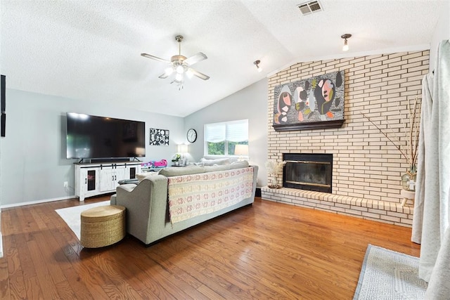 815 W 7th St, Edmond, OK 73003 - living room featuring ceiling fan, wood finished floors, lofted ceiling, a brick fireplace, and a textured ceiling