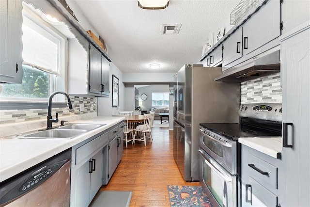 815 W 7th St, Edmond, OK 73003 - kitchen with stainless steel appliances, under cabinet range hood, a textured ceiling, light wood-style floors, and tasteful backsplash