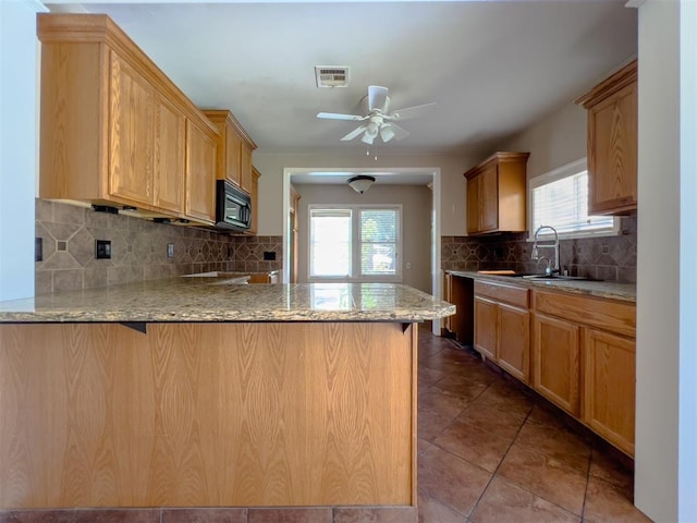 2437 NW 36th Ter, Oklahoma City, OK 73112 - kitchen featuring black microwave, a peninsula, a ceiling fan, tasteful backsplash, and light stone countertops