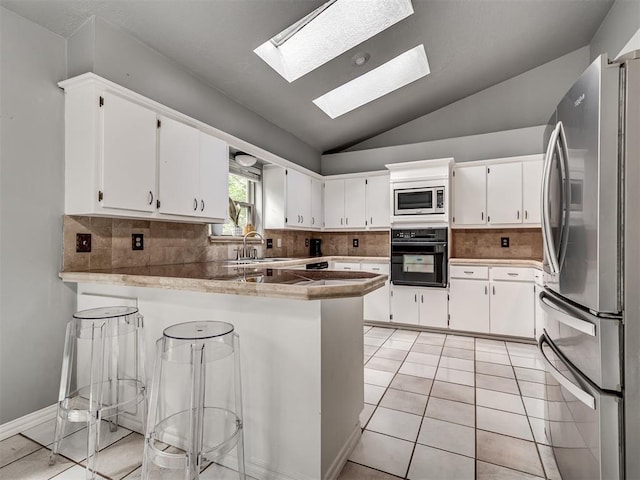 5101 Long Branch Ln, Edmond, OK 73034 - kitchen with stainless steel appliances, a peninsula, vaulted ceiling, white cabinets, and a skylight