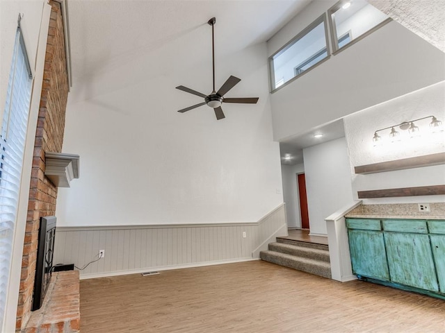 1404 Mary Lee Ln, Edmond, OK 73034 - unfurnished living room featuring a high ceiling, wood finished floors, a ceiling fan, a fireplace, and wainscoting