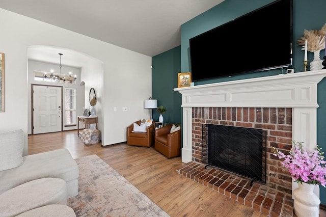 18200 Allora Dr, Edmond, OK 73012 - living area featuring wood finished floors, a chandelier, a brick fireplace, arched walkways, and vaulted ceiling