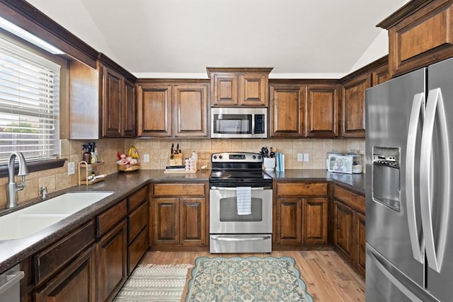18200 Allora Dr, Edmond, OK 73012 - kitchen featuring stainless steel appliances, vaulted ceiling, light wood-style floors, tasteful backsplash, and dark countertops