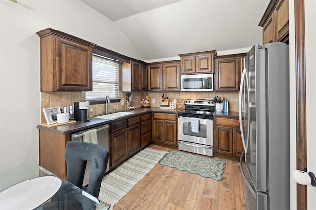 18200 Allora Dr, Edmond, OK 73012 - kitchen featuring stainless steel appliances, vaulted ceiling, light wood-style flooring, dark countertops, and decorative backsplash
