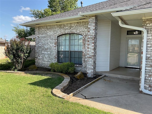 10201 Pinckney Ct, Oklahoma City, OK 73162 - property entrance with roof with shingles, a yard, and brick siding