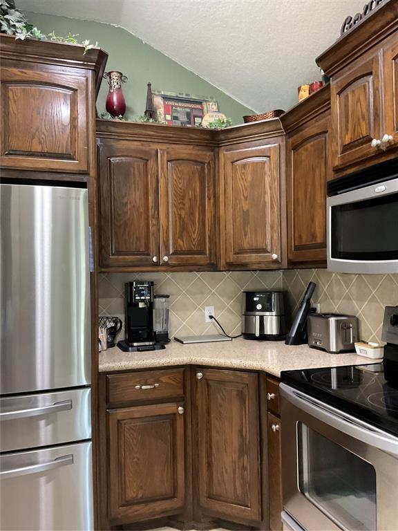 10201 Pinckney Ct, Oklahoma City, OK 73162 - kitchen featuring appliances with stainless steel finishes, vaulted ceiling, backsplash, light countertops, and a textured ceiling
