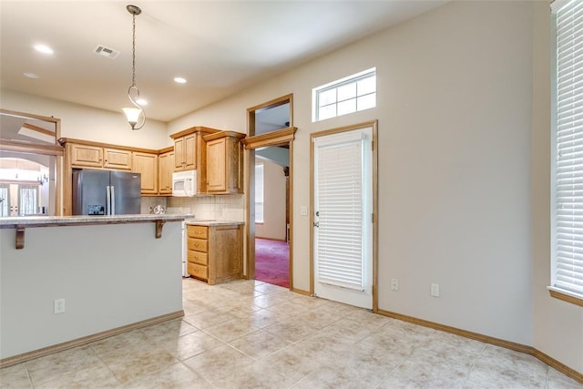 1308 River Birch Dr, Yukon, OK 73099 - kitchen featuring stainless steel refrigerator with ice dispenser, white microwave, tasteful backsplash, light countertops, and decorative light fixtures