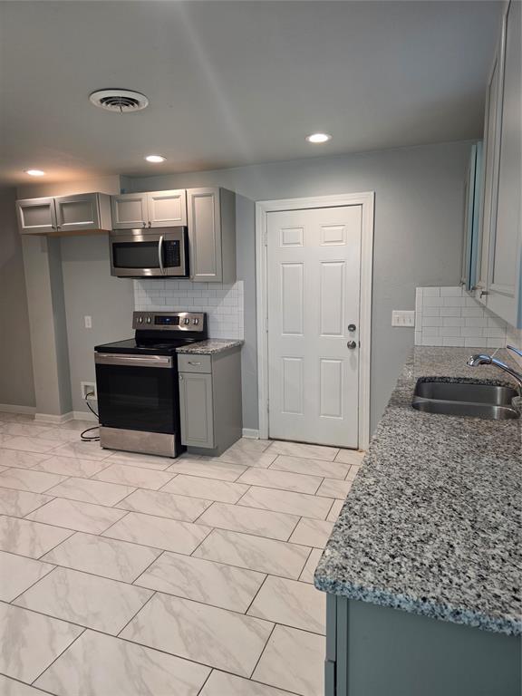 6101 NW 48th St, Warr Acres, OK 73122 - kitchen featuring appliances with stainless steel finishes, gray cabinetry, tasteful backsplash, light stone counters, and light marble finish flooring