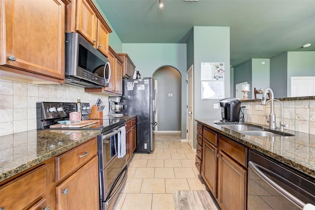 2500 SE 93rd St, Moore, OK 73160 - kitchen featuring stainless steel appliances, arched walkways, brown cabinetry, backsplash, and dark stone countertops