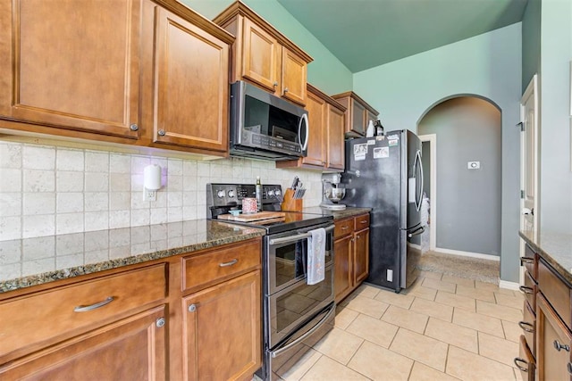 2500 SE 93rd St, Moore, OK 73160 - kitchen with stainless steel appliances, brown cabinets, arched walkways, dark stone counters, and backsplash
