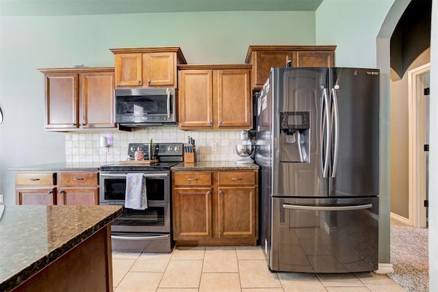 2500 SE 93rd St, Moore, OK 73160 - kitchen featuring stainless steel appliances, dark stone countertops, arched walkways, backsplash, and brown cabinetry