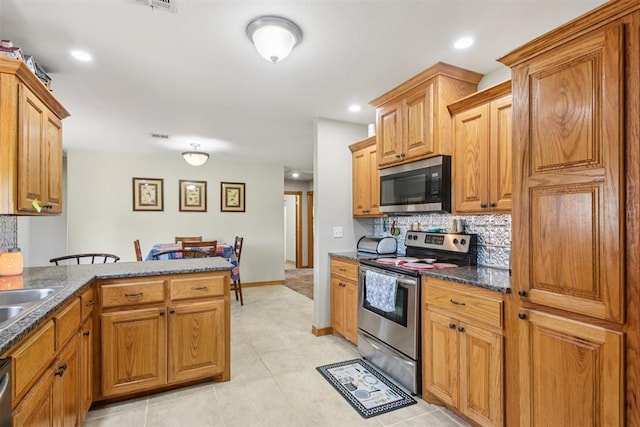 720 N Main St, Blanchard, OK 73010 - kitchen with appliances with stainless steel finishes, tasteful backsplash, a peninsula, light tile patterned flooring, and brown cabinets