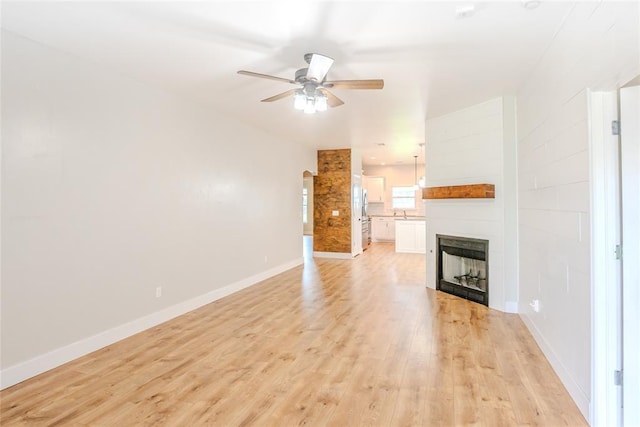 621 SW 7th St, Moore, OK 73160 - unfurnished living room featuring ceiling fan, light wood finished floors, a fireplace, and arched walkways