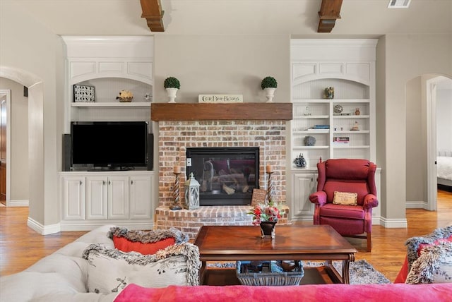 2725 Open Range Rd, Edmond, OK 73034 - living room with built in features, arched walkways, light wood-style floors, and a brick fireplace