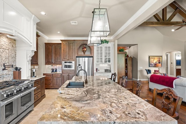 2725 Open Range Rd, Edmond, OK 73034 - kitchen featuring appliances with stainless steel finishes, tasteful backsplash, light stone countertops, a large island, and arched walkways