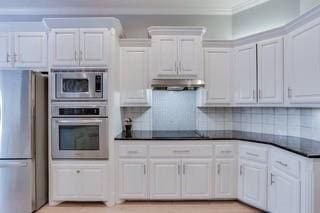 17009 Wales Green Ave, Edmond, OK 73012 - kitchen with stainless steel appliances, under cabinet range hood, dark countertops, white cabinetry, and crown molding