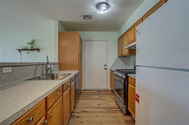 2013 Creekridge Dr, Oklahoma City, OK 73141 - kitchen featuring freestanding refrigerator, stainless steel gas range, under cabinet range hood, brown cabinetry, and light wood-style flooring