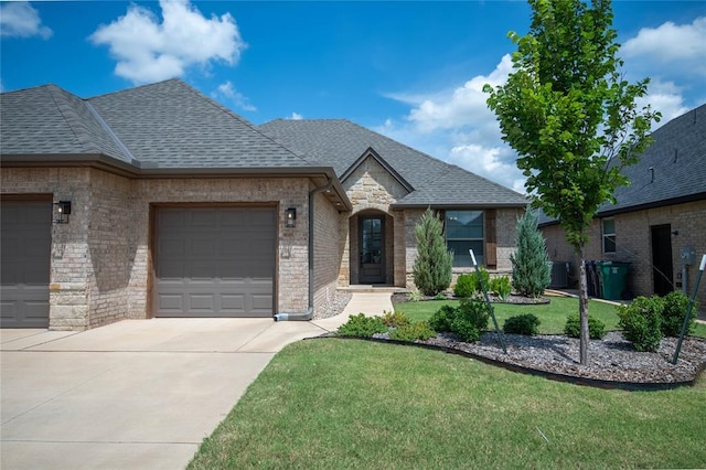 14704 Ashore Dr, Oklahoma City, OK 73142 - french country style house with an attached garage, concrete driveway, a shingled roof, brick siding, and a front yard