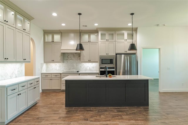 14704 Ashore Dr, Oklahoma City, OK 73142 - kitchen featuring appliances with stainless steel finishes, premium range hood, a kitchen island with sink, decorative backsplash, and dark wood-type flooring