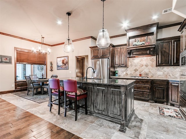 17401 Melville Ln, Edmond, OK 73012 - kitchen featuring appliances with stainless steel finishes, ornamental molding, tasteful backsplash, a chandelier, and a kitchen island with sink