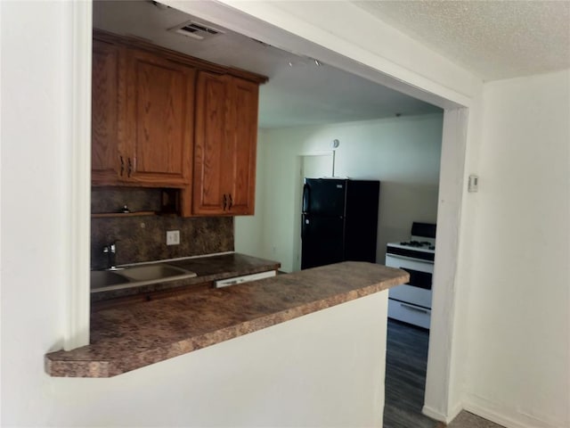 116 SE 39th St, Oklahoma City, OK 73129 - kitchen with white gas range, freestanding refrigerator, brown cabinetry, dark countertops, and a textured ceiling