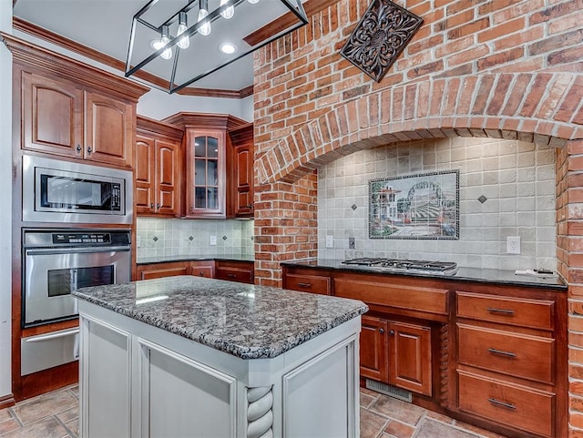 1217 Camelot Dr, Yukon, OK 73099 - kitchen featuring ornamental molding, stone tile flooring, appliances with stainless steel finishes, dark stone countertops, and tasteful backsplash