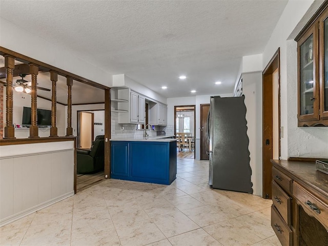 6105 W Gun Hill Way, Warr Acres, OK 73132 - kitchen featuring freestanding refrigerator, glass insert cabinets, a peninsula, a textured ceiling, and a ceiling fan