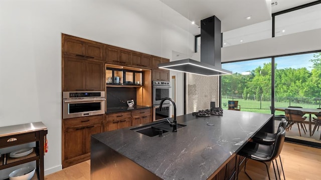 10105 SW 25th Ct, Yukon, OK 73099 - kitchen featuring light wood-style flooring, island exhaust hood, stainless steel double oven, a kitchen breakfast bar, and dark stone counters