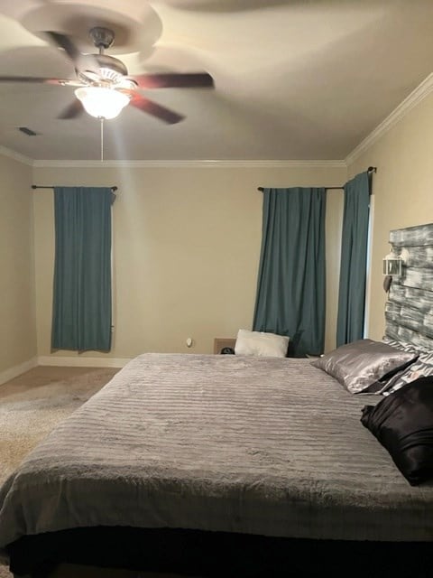 carpeted bedroom with visible vents, ornamental molding, ceiling fan, and baseboards