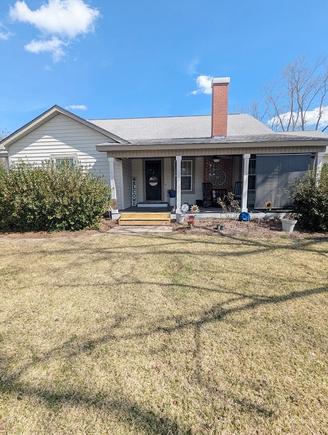 back of property featuring covered porch, a yard, and a chimney