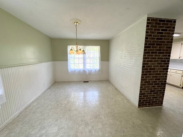 2403 Stonebridge Rd, Dothan, AL 36301 - unfurnished dining area with a chandelier, wainscoting, brick wall, light floors, and a textured ceiling