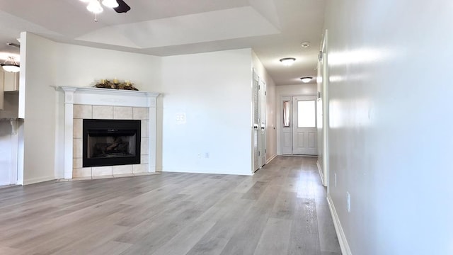 unfurnished living room featuring baseboards, light wood finished floors, a tiled fireplace, and a ceiling fan